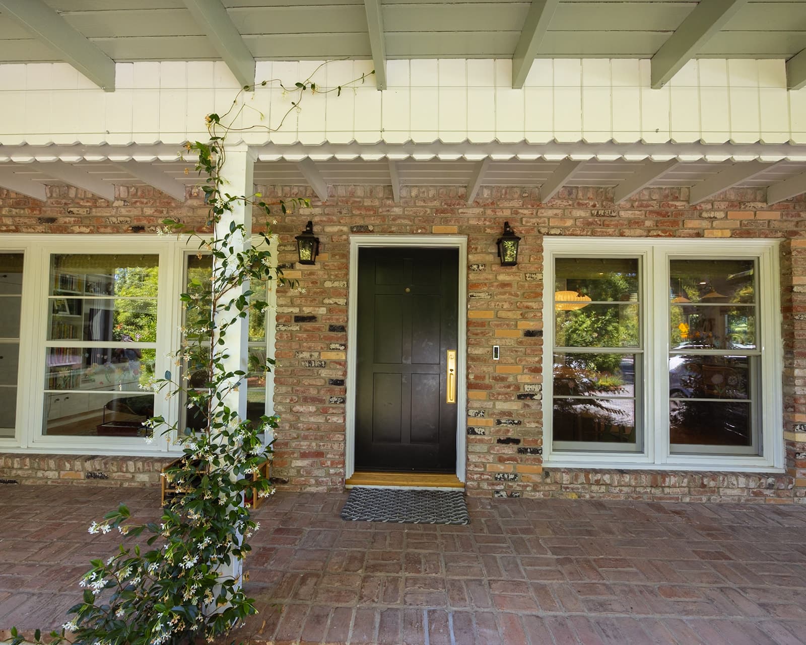 Covered front porch running along the brick facade and green-trimmed windows