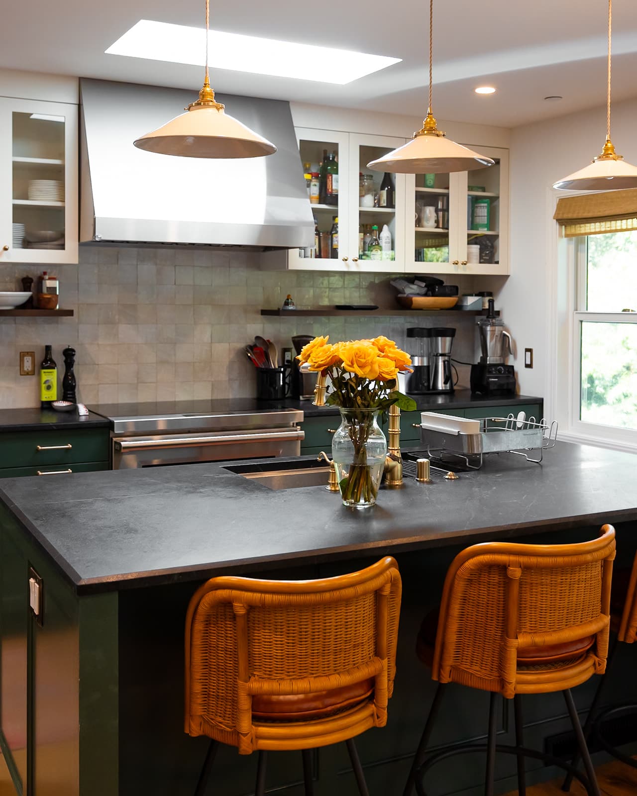 Honed soapstone kitchen island with rattan counter stools and brass pendant lights