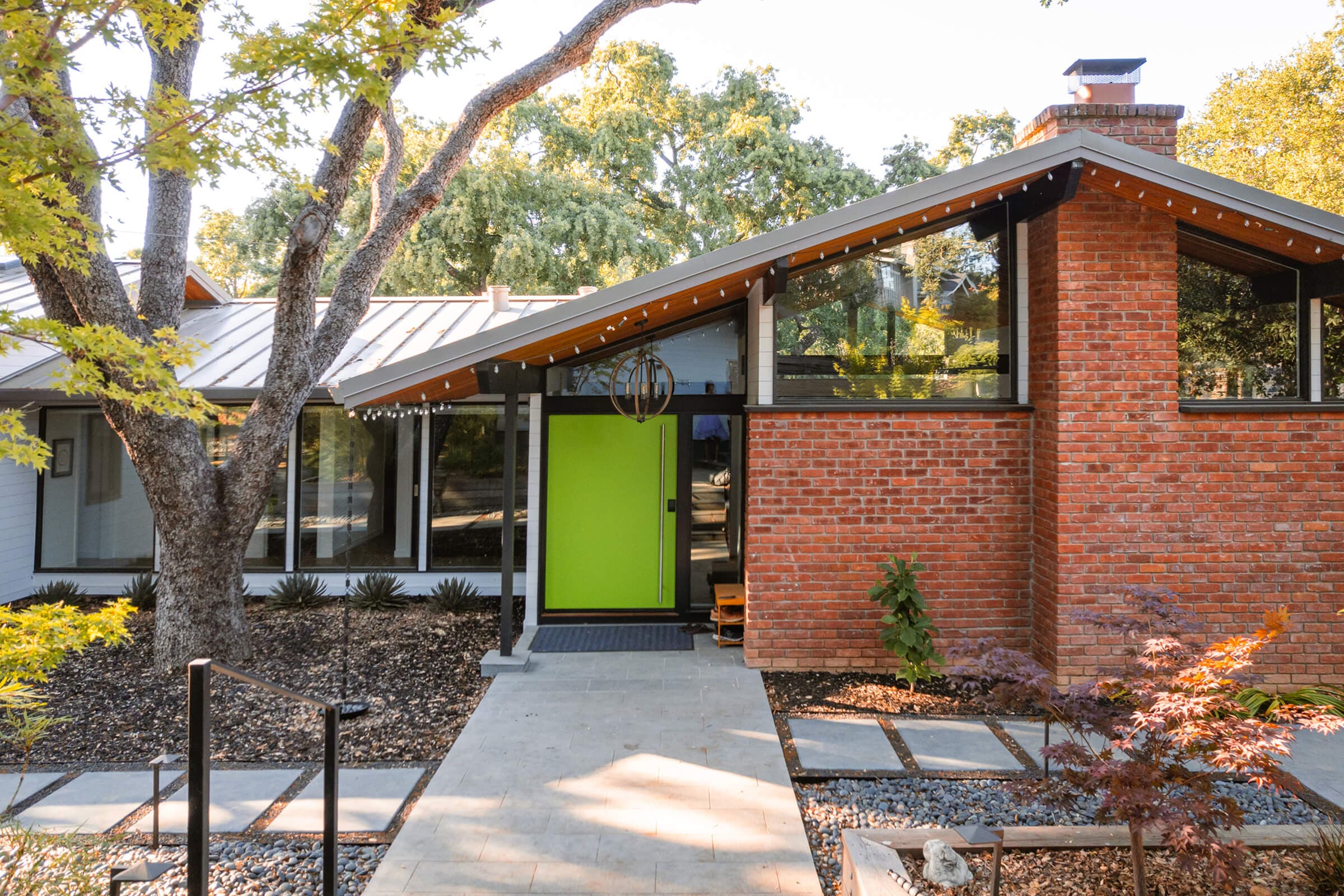 Front of the 1967 Los Gatos home with a lime-green front door, brick chimney wall, and clerestory windows