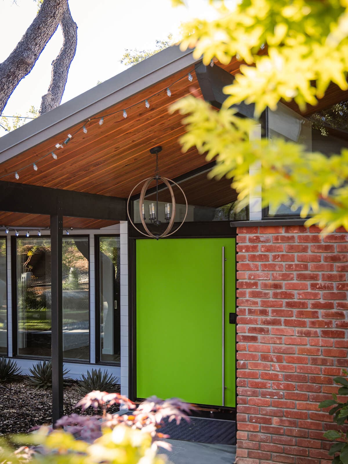 Lime-green front door beneath a wood soffit beside the brick chimney